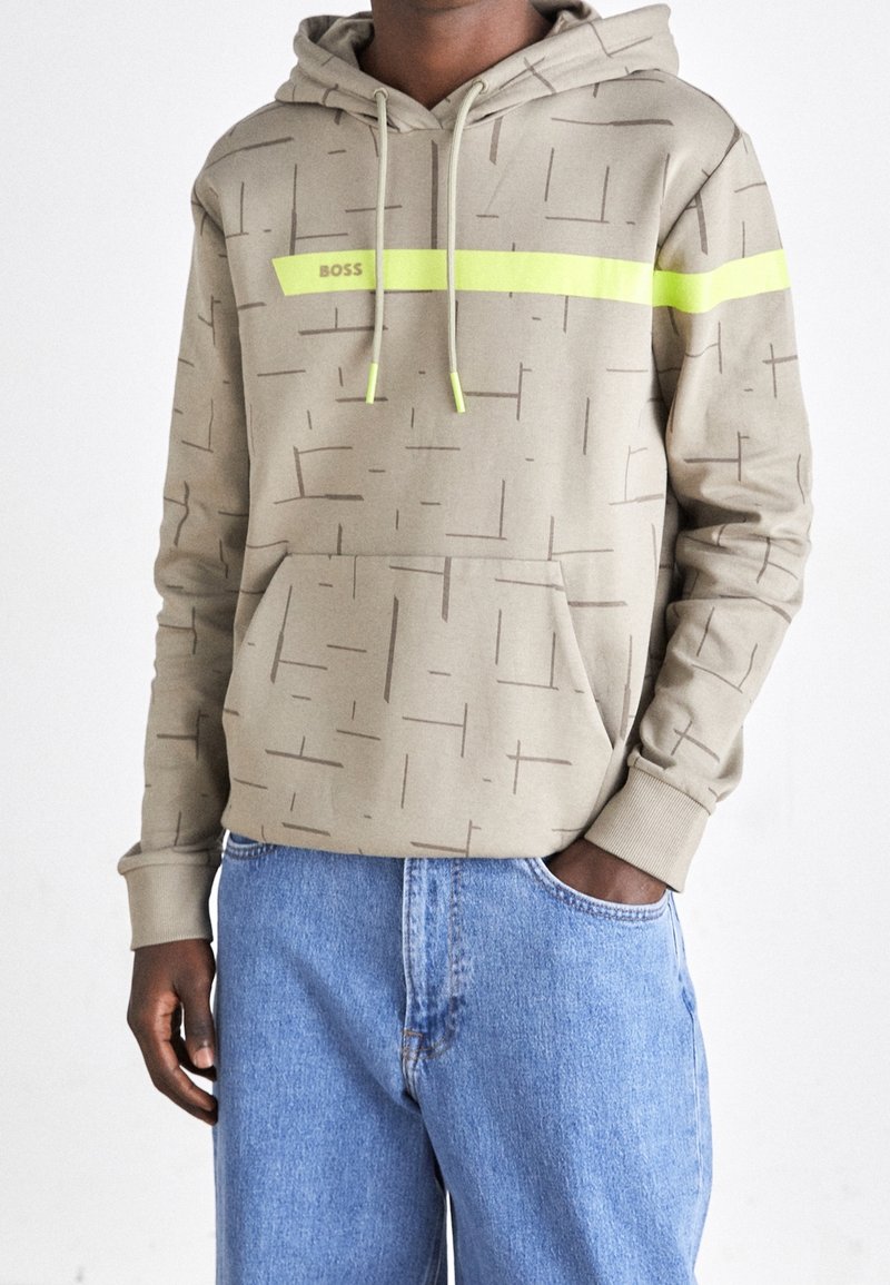 Beige hoodie med tonala geometriska mönster, neongrön accentrand, justerbara dragsnören och en framficka i kengurustil.