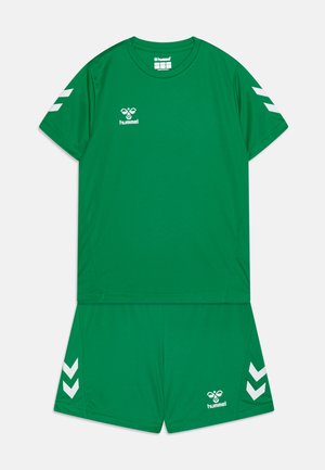 Grünes Sportset aus leichtem Stoff; enthält ein kurzärmliges Shirt und Shorts mit weißen Chevron-Akzenten und Branding.