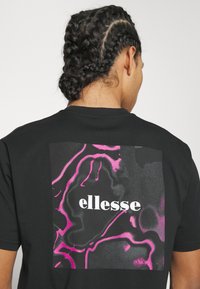 Black t-shirt featuring a large graphic on the back in black and pink swirls with "ellesse" in white bold font. Short sleeves, standard fit.