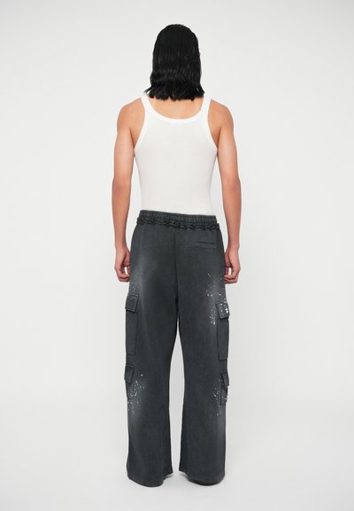 Sivé cargo nohavice s voľným strihom, sťahovacím pásom, viacerými bočnými vreckami a bodkovanou textúrou. Skombinované s bielym tielkom.