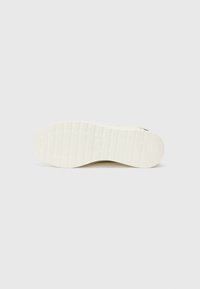 Suola della scarpa in bianco sporco con un motivo testurizzato e scanalature per una migliore aderenza, che presenta una forma arrotondata e un design liscio e pulito.