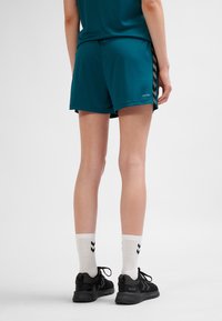 Turkosa sportshorts med avslappnad passform, med ett mönster på sidan och svarta detaljer. Kombineras med vita strumpor och svarta sneakers.