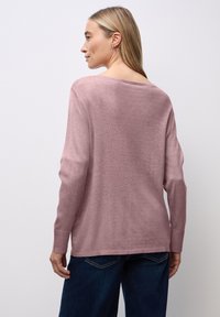Maglione a pullover rosa chiaro con maniche lunghe e scollatura ampia, caratterizzato da una morbida consistenza e dettagli a coste sull'orlo. Indossato con jeans blu scuro.