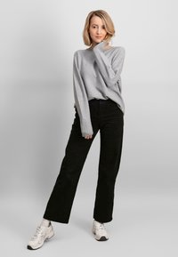 Maglione grigio chiaro con vestibilità ampia e maniche lunghe, abbinato a pantaloni neri a gamba larga e sneakers bianche. Design semplice, con dettagli minimi.