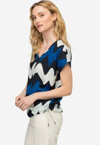 Top astratto blu e bianco con scollo a V e maniche corte, caratterizzato da un orlo arricciato con coulisse regolabile.