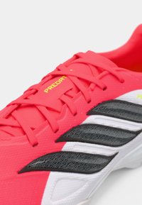 Φωτεινό ροζ ποδοσφαιρικό παπούτσι με μαύρες και λευκές λεπτομέρειες, υφασμάτινη επιφάνεια και κίτρινο λογότυπο "PREDATOR". Διαθέτει ροζ κορδόνια που ταιριάζουν.