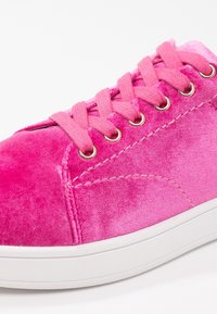 Baskets en velours rose avec une texture lisse, dotées de lacets rose clair, d'œillets métalliques ronds et d'une semelle en caoutchouc blanche.