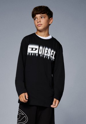 T-shirt a maniche lunghe nera con logo grafico bianco "DIESEL" con effetti sfumati. Design semplice con colletto a girocollo, abbinato a pantaloni neri.