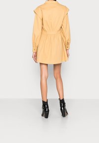 Korte mouwen, gebeld jurk van lichtgele katoen, met knoopmanchetten en een geplooide taille. G gedragen met zwarte enkellaarsjes met hak.