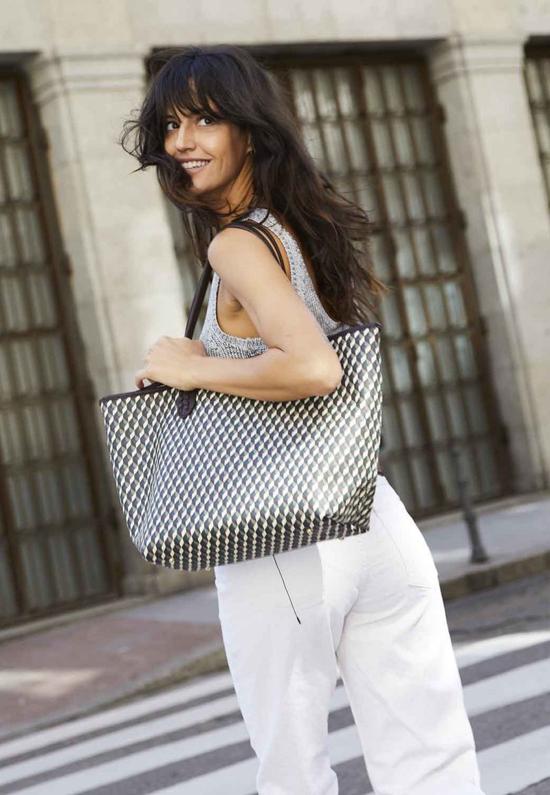 Woven tote bag featuring a geometric black and white pattern, sturdy handles, spacious design, and a textured finish.
