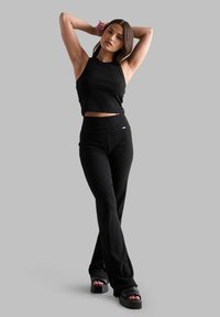 Schwarzes geripptes Crop-Top, kombiniert mit hochgeschnittenen schwarzen Hosen. Das Outfit hat eine glatte Textur und wird durch klobige schwarze Sandalen ergänzt.