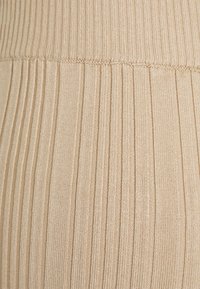 Tecido de malha canelada bege apresentando riscas verticais, com uma textura suave e um design de cintura larga.