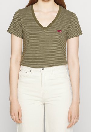 Person iført en olivengrøn og hvidstribet V-hals Levi's t-shirt med korte ærmer og hvide bukser med høj talje.