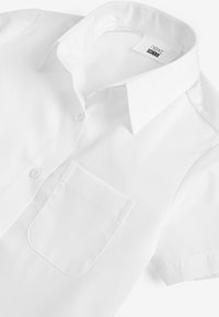Chemise blanche à manches courtes en tissu lisse avec un plastron à boutons et une poche poitrinière gauche. Caractérisée par un col à la coupe nette.