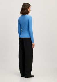 Lichtblauw geribd langdannelse topje gecombineerd met zwarte wijde pijpen broek. Het topje heeft een ronde halslijn en een getailleerde pasvorm.