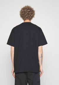 Camiseta de algodón negra de manga corta, con corte relajado y escote redondo. La parte de atrás es lisa, sin logotipos ni estampados.