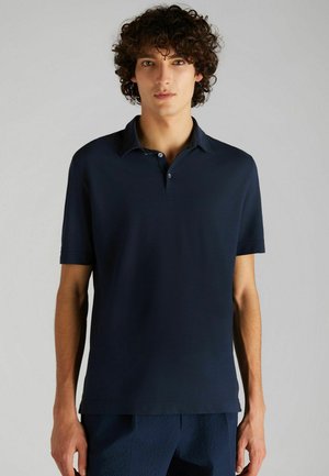 Polo bleu marine avec un col court, trois boutons et des manches courtes. Confectionné en tissu lisse avec une coupe ajustée.