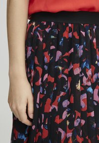 Zwarte geplooide rok met een kleurrijk abstract patroon in rood, roze en blauw. De tailleband is effen zwart en glad.