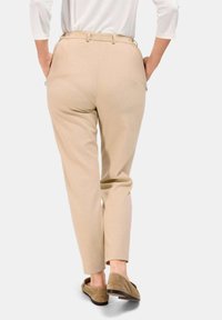 Beige Hosen mit taillierter Passform, mittelhoher Taille, seitlichen Taschen und einer glatten Textur. Kombiniert mit braunen Slippern.