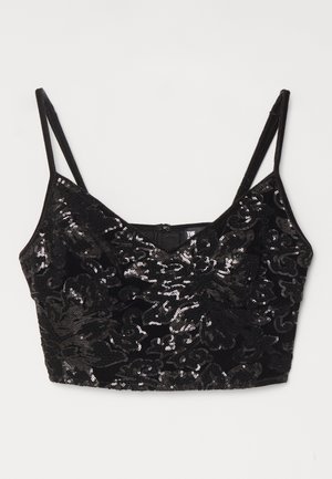 Crop top en sequins noirs avec un motif texturé, décolleté en V, fines bretelles ajustables et fermeture éclair au dos. Surface brillante qui reflète la lumière.