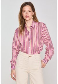 Camicia con bottoni caratterizzata da righe verticali in rosa, viola, crema e beige. Maniche lunghe con polsini, abbinata a pantaloni chiari.
