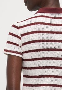 Strikket polo-skjorte med horisontale burgunder- og hvite striper, laget av et teksturert stoff og med en ensfarget burgunder krage. Korte ermer.