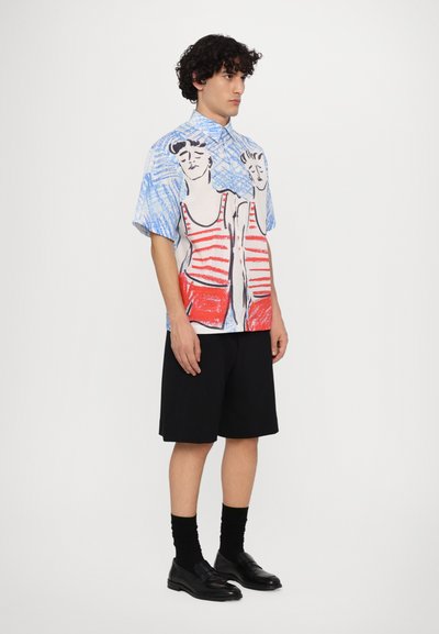 Camisa de manga corta con un fondo estampado en azul y blanco que presenta figuras a rayas rojas. Combinada con pantalones cortos y zapatos negros.