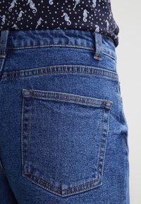 Dżinsy ze skóry denim w ciemnym granatowym kolorze, z klasycznym, pięciokieszeniowym krojem. Charakteryzują się widocznym przeszyciem i standardowym kształtem tylnych kieszeni.