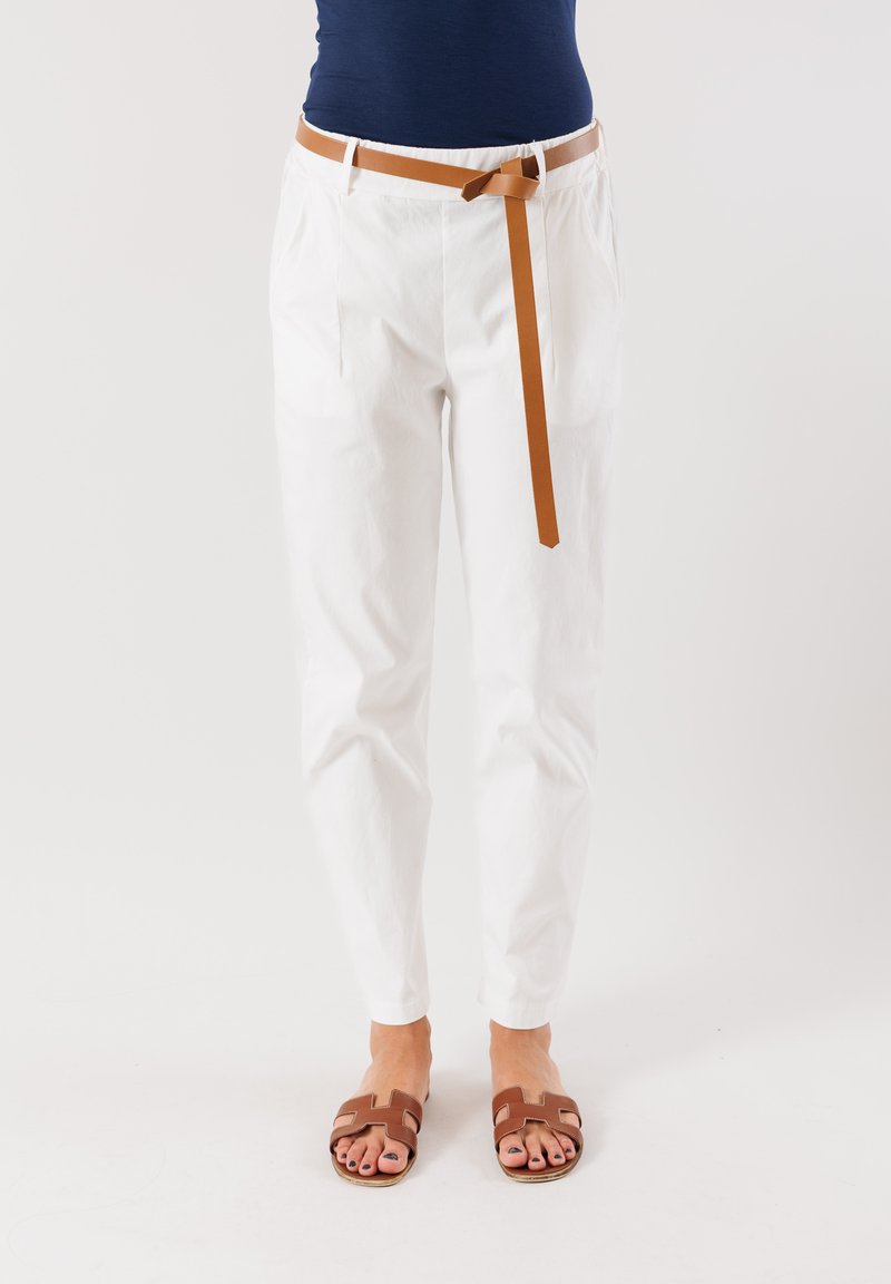 Pantaloni bianchi affusolati con tasche laterali, cintura elastica e cintura marrone. Abbinati a sandali marroni con design ritagliato.