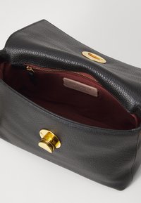 Sac à main en cuir noir avec une finition texturée, quincaillerie dorée et doublure intérieure bordeaux. Il présente un fermoir magnétique et une poche zippée.