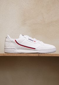 Fehér bőr sneaker piros és kék színű díszcsíkokkal, strukturált oldalsó panellel, valamint logó részletekkel a nyelven és a saroknál. Lapos gumi talp.