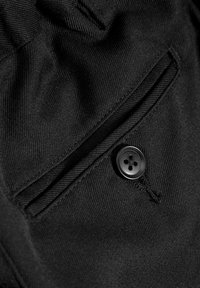 Tissu noir avec une surface texturée, comprenant une petite poche à rabat et un bouton noir à quatre trous sur le côté.