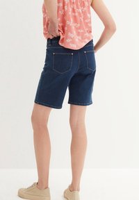 Mörkblå jeansshorts med regular fit, femficksdesign och upprullad fåll. Bärs med en rosa blommig blus och beige sneakers.