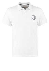 Polo de manga corta blanco hecho de algodón, con un cierre de dos botones y un logo de escudo bordado en el lado izquierdo del pecho.