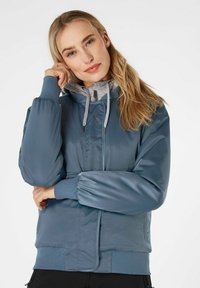Giacca blu imbottita con zip anteriore, rivestimento interno della cappuccio grigio, polsini elasticizzati e tasche laterali. Tessuto liscio e lucido con dettaglio trapuntato.