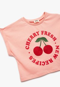 Camiseta de manga corta rosa con cerezas rojas bordadas y el texto "RECETAS NUEVAS FRESCAS DE CEREZA" en un diseño circular. Material suave de algodón.