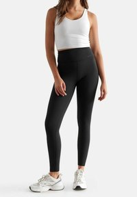 Leggings neri a vita alta realizzati in tessuto elasticizzato, abbinati a un crop top bianco e scarpe da ginnastica bianche, adatti per gli allenamenti.