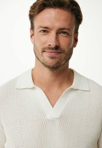 Pullover bianco lavorato a maglia con scollo a V e colletto corto. Presenta una trama a maglia aperta, creando un aspetto leggero e traspirante.