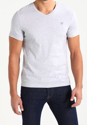 Homme portant un t-shirt à col en V gris clair à manches courtes avec un petit logo sur la poitrine, associé à un jean bleu foncé.