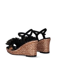 Sandalias de cuña negras con tacones de paja trenzada, que cuentan con un adorno floral en la parte frontal y correas ajustables en el tobillo.