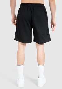 Svarta träningsshorts med ett strukturerat mönster, elastisk midja och sidofickor, kombinerat med vita strumpor och sneakers.