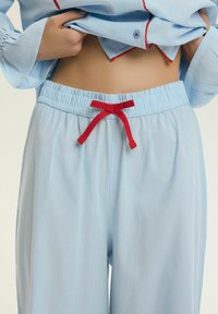 Luźne jasnoniebieskie spodnie z elastycznym pasem i czerwonym sznurkiem zawiązanym na kokardę, noszone z dopasowanym górym podniesionym, odsłaniającym brzuch.