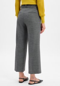 Graue, strukturierte Hose mit lockerer Passform, geradem Schnitt und Gesäßtasche, kombiniert mit schwarzen Slippern.