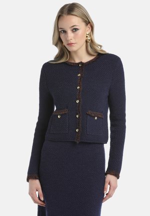 Navy knit jacket with a textured finish, gold buttons, and brown accent trimming along the neckline and pockets. Features two front pockets.