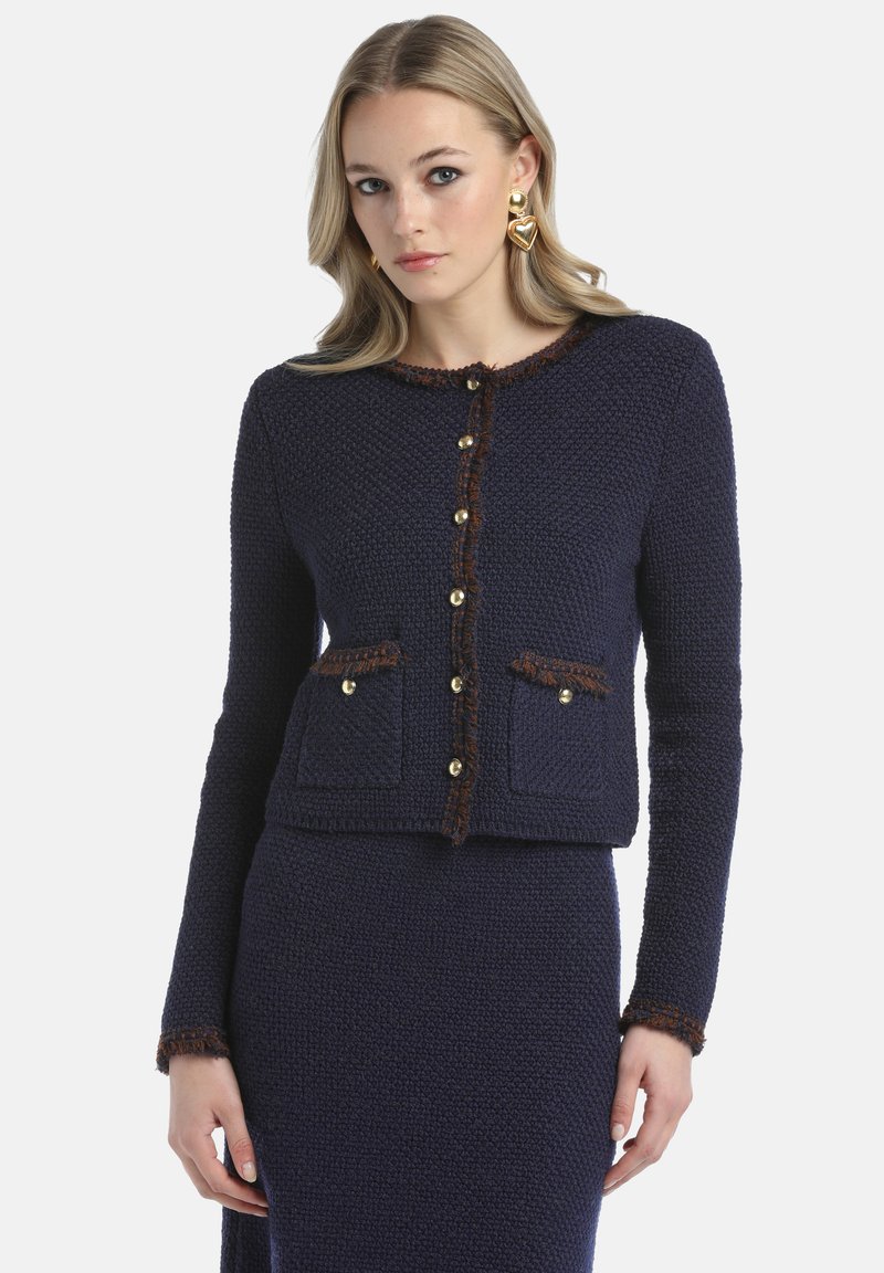 Navy knit jacket with a textured finish, gold buttons, and brown accent trimming along the neckline and pockets. Features two front pockets.