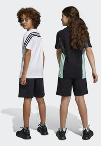 Due bambini in uniforme sportiva si trovano schiena contro schiena. Uno indossa una maglietta bianca con strisce nere; l'altro ha una maglietta nera e verde chiaro.