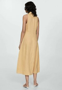 Vestito senza maniche, lungo fino al ginocchio, in tessuto giallo chiaro. Caratterizzato da un collo alto e una vestibilità morbida, con una forma a trapezio e una texture sottile.