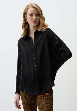 Black, long-sleeve blouse in silky fabric with a buttoned front and relaxed fit. Paired with animal print trousers.