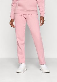 Roze katoenen joggers met een slim fit, voorzien van een wit logo op de linkerdij en ribgebreide boorden bij de enkels. Gecombineerd met witte sportschoenen.