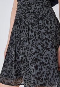 Flödig svart och grå kjol med prickig djurtryck, gathered midja, bärs av en person med nakna armar synliga.